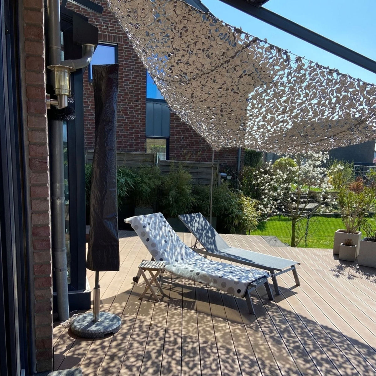 Filet de camouflage triangulaire gris au-dessus d'une terrasse avec transats